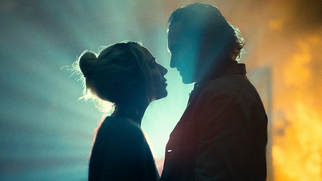Lady Gaga as Lee and Joaquin Phoenix as Arthur standing silhouetted in front of a projector in Joker: Folie á Deux.